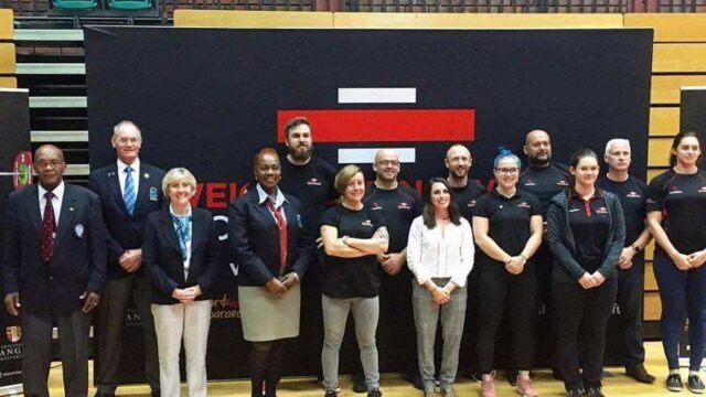 Volunteers Officials stood in front of large Weightlifting Wales logo banner