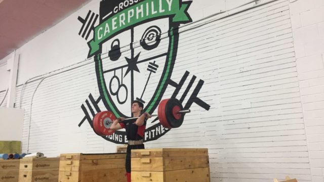 Athlete jerking from blocks in front of large Caerphilly Club logo painted on the wall